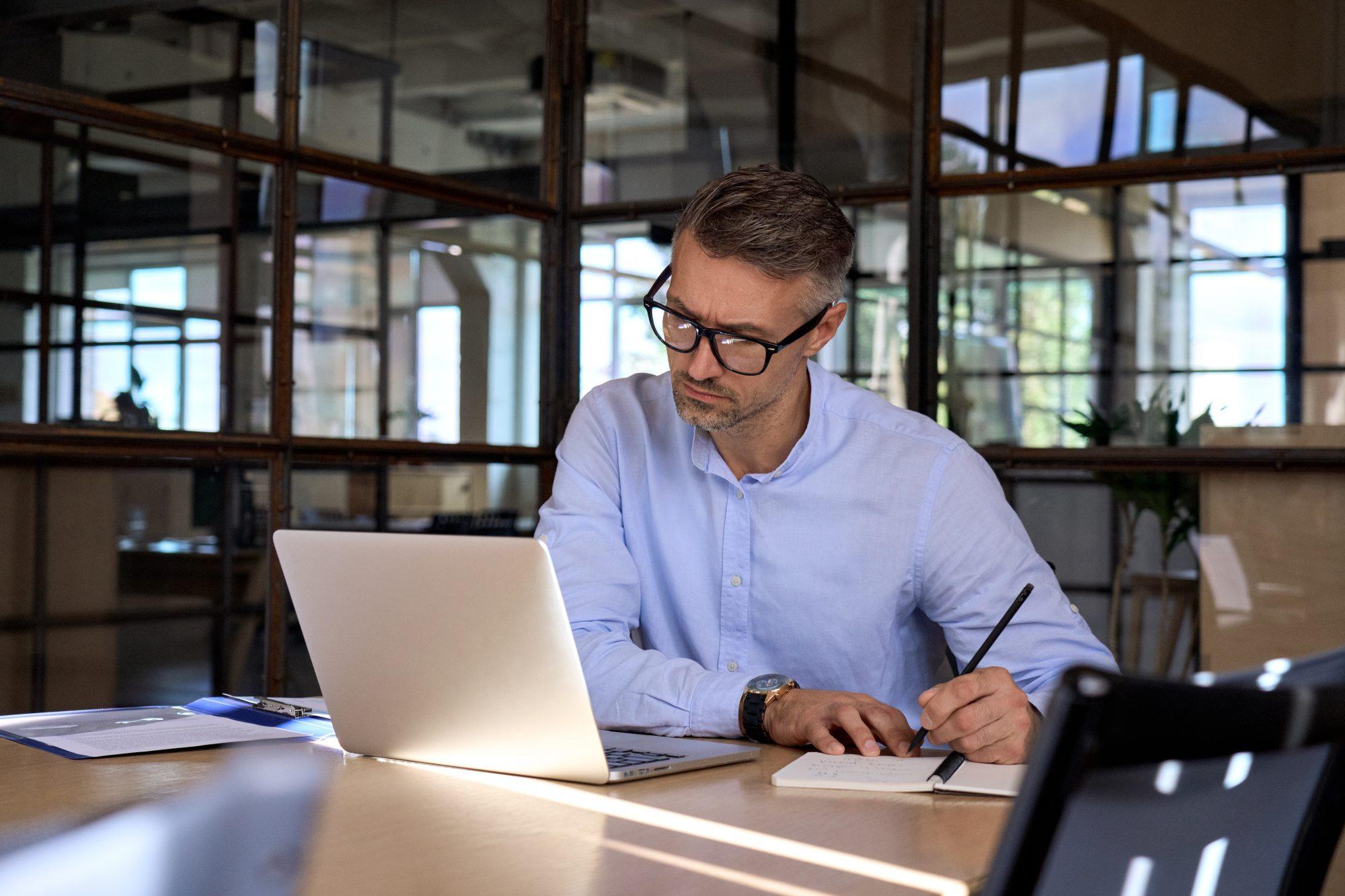 Mature business man manager looking at laptop watching online webinar in office.